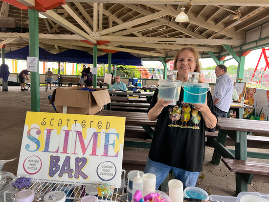 Woman holding slime containers at a Slime Bar event under an outdoor shelter.
