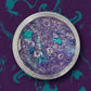 Purple glitter with blue and clear beads in a clear container on a brown surface