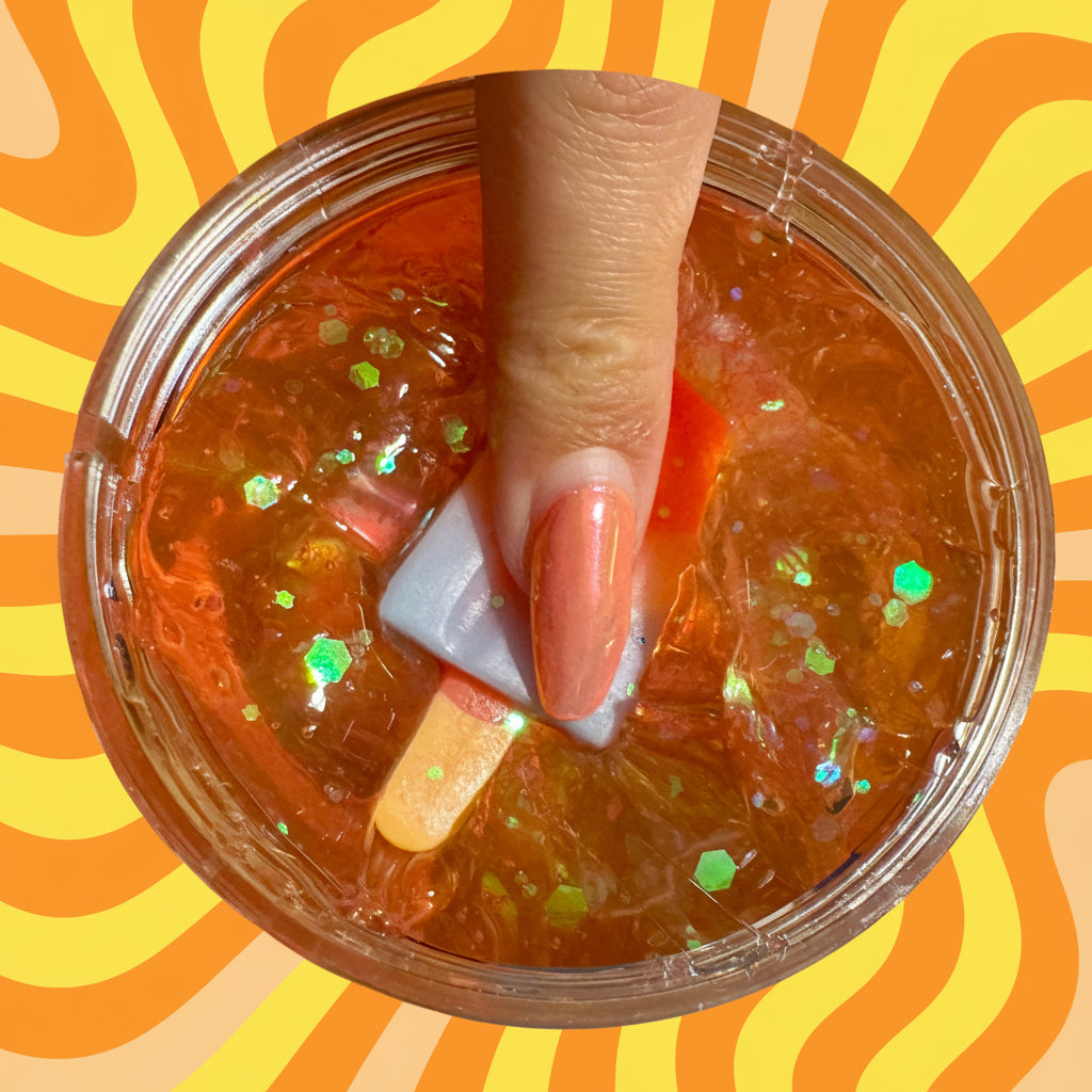 Hand holding a small popsicle over a container of jelly with shimmer sprinkles